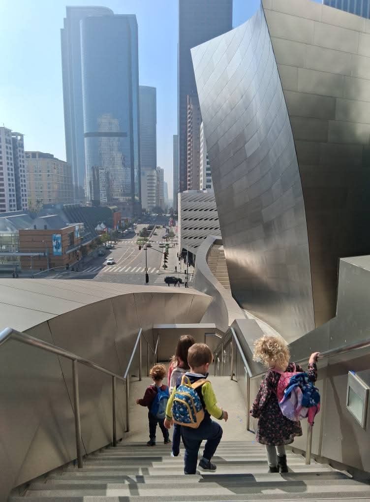 Four children with backpacks heading down the steps below Walt Disney Concert Hall, the downtown Los Angeles skyline ahead